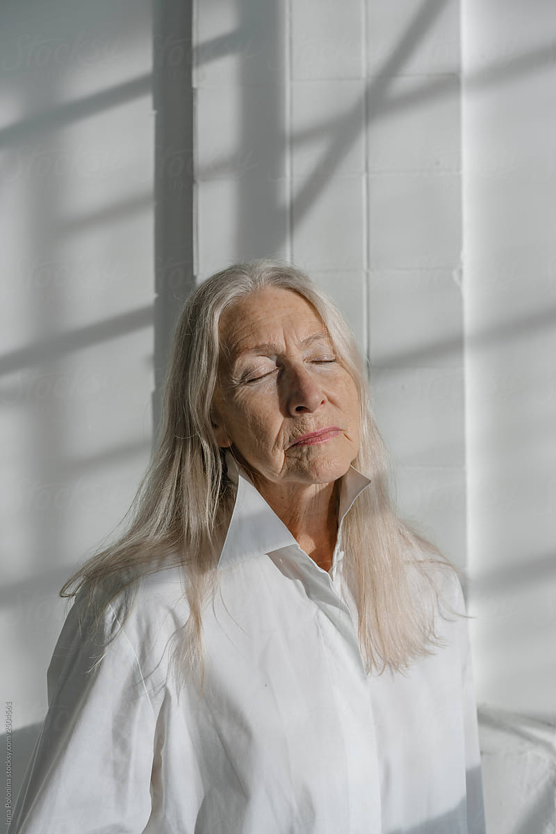 Portrait of a senior woman with grey long hair in white modern studio