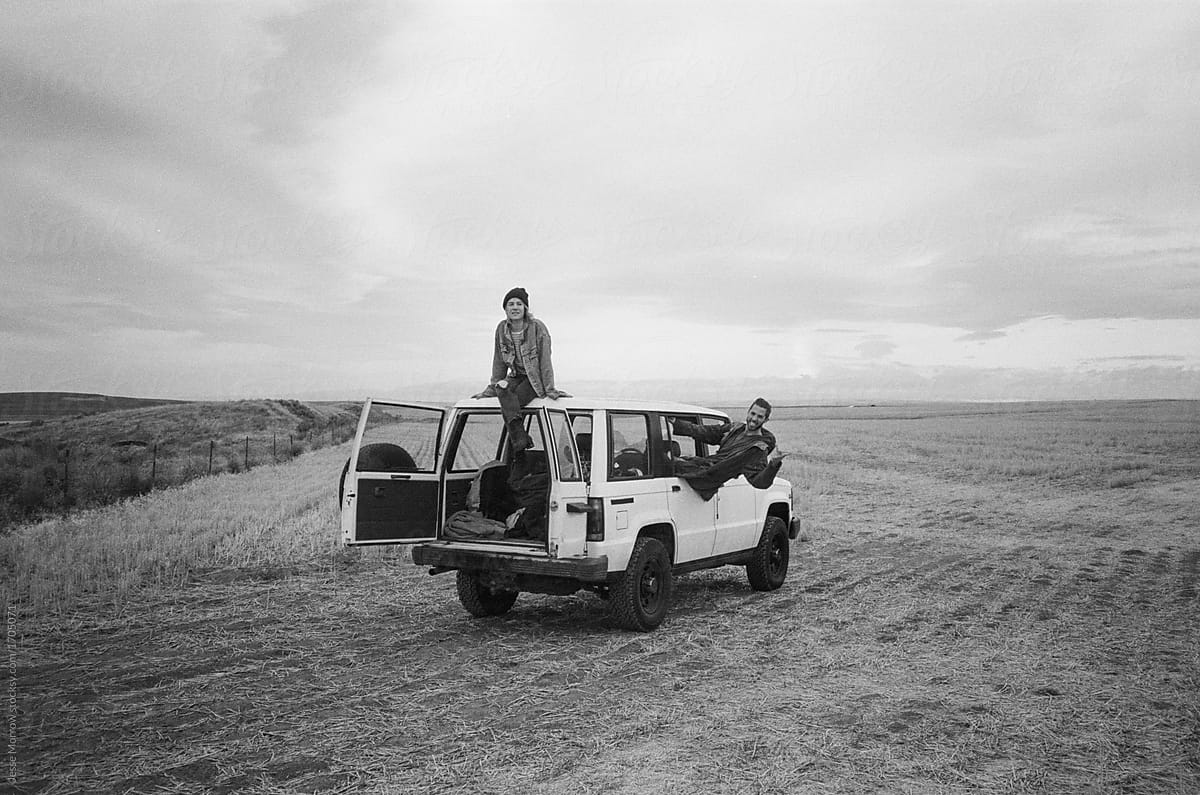 Lifestyle image of male and female sitting on top of suv truck in field on off road adventure