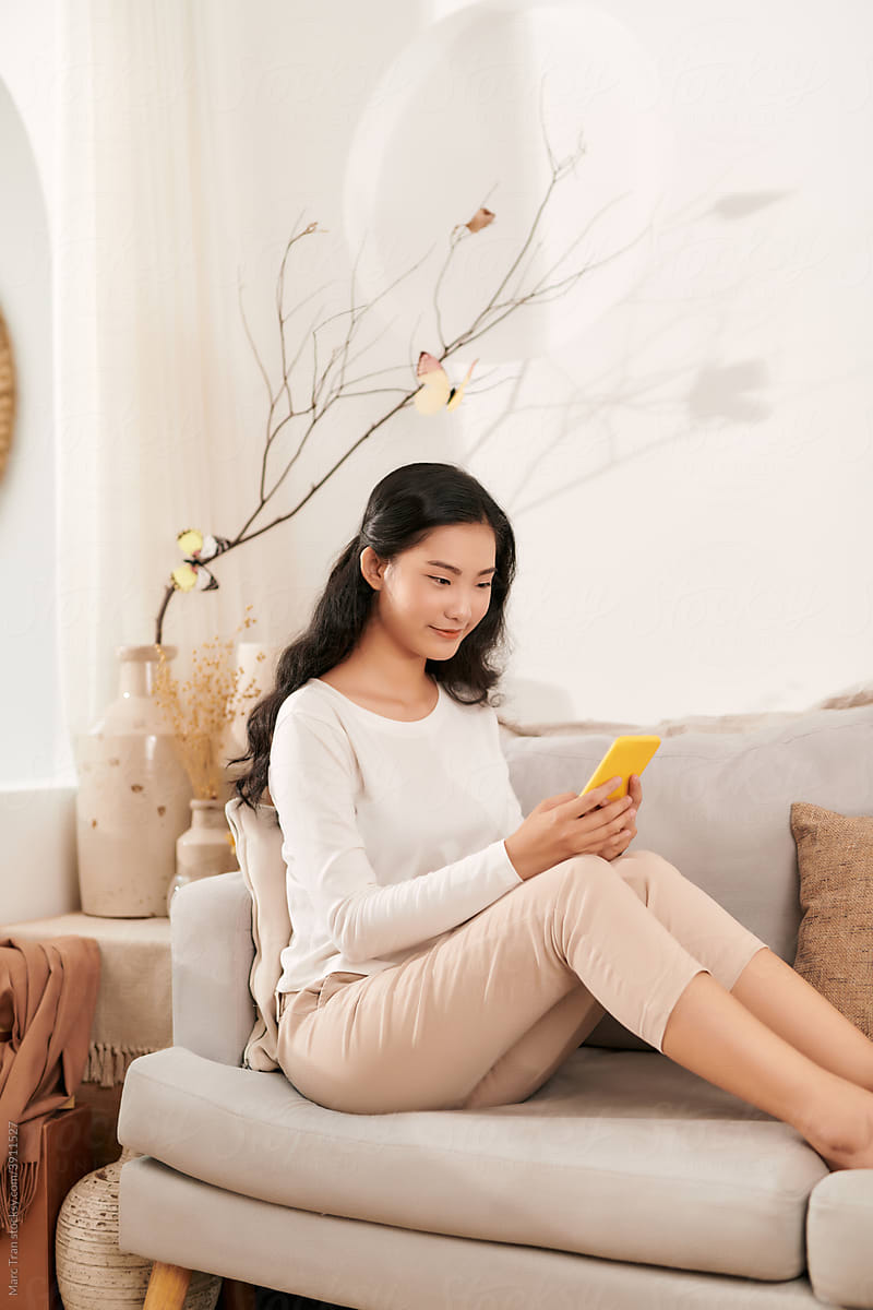 young happy woman using mobile phone on sofa