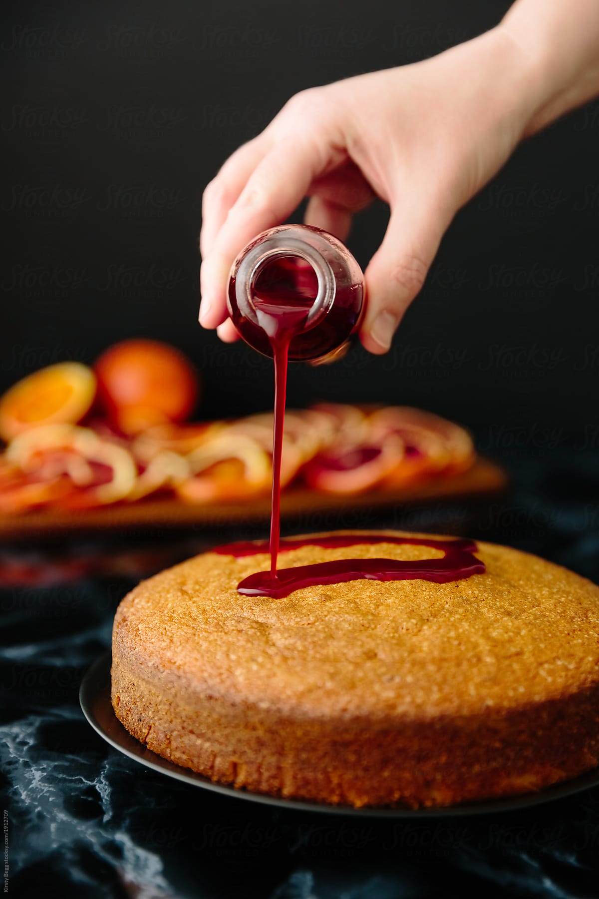 Woman pouring red orange syrup glaze onto cake