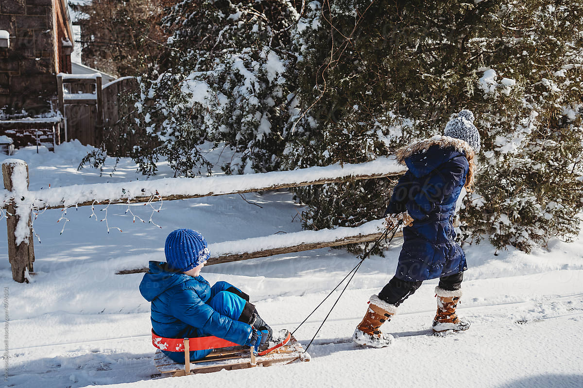A girl pulls her brother on a sled.