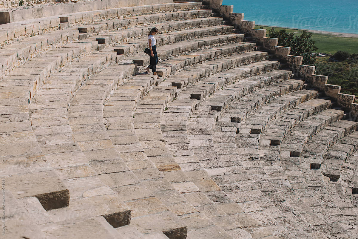 Stylish woman running by  stairs of amphitheater in sunny weather