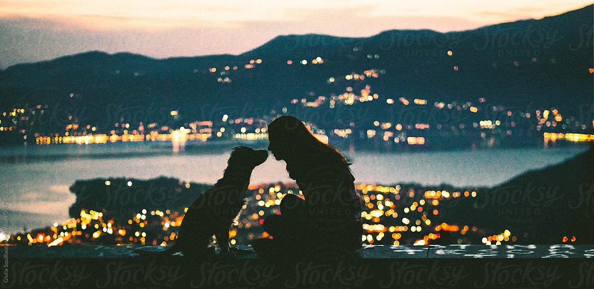 Girl and dog kissing with the city lights at the background