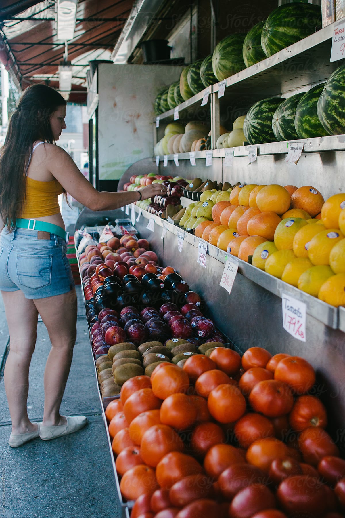 young woman looking at fresh fruit at an open street store