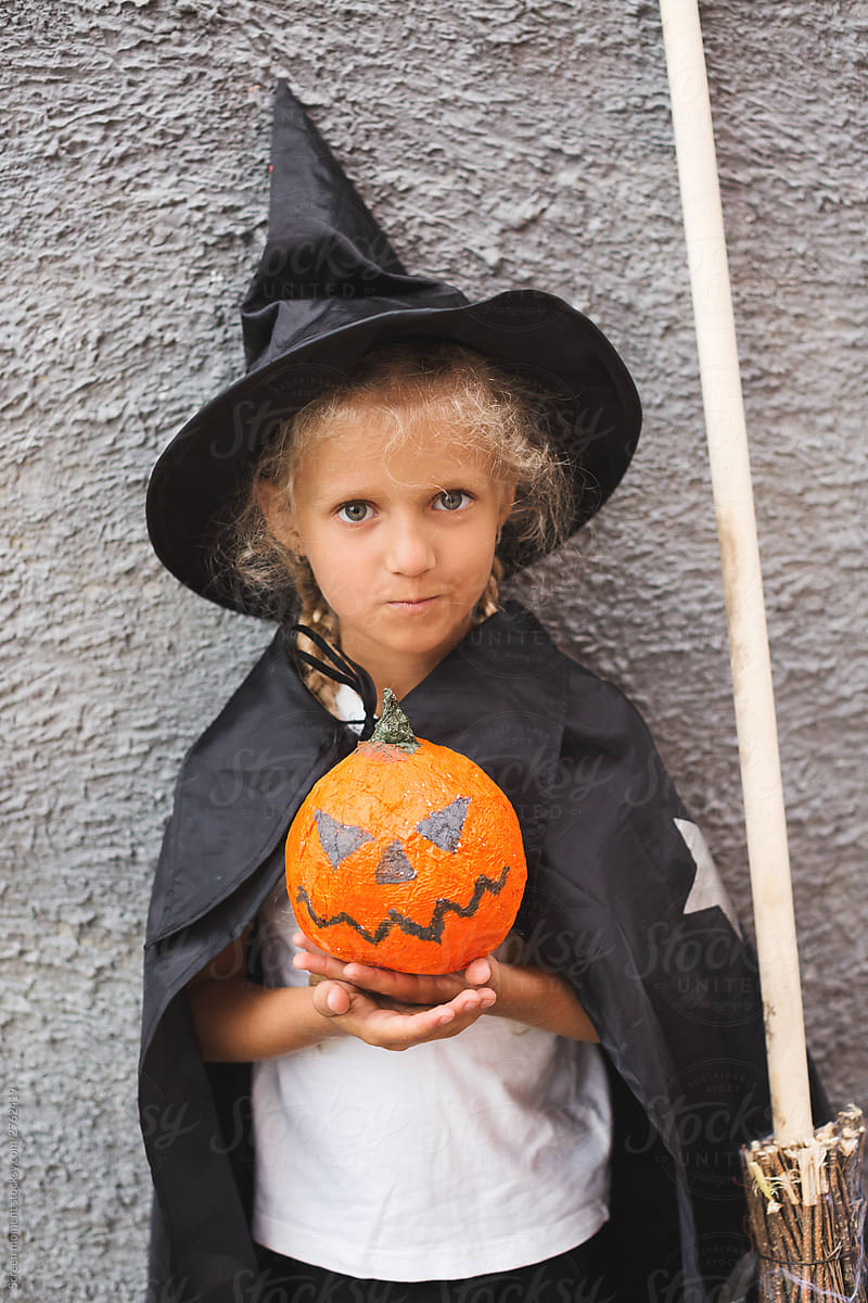 Girl in Halloween costume having fun. A little girl in a witch costume is playing with a pumpkin.