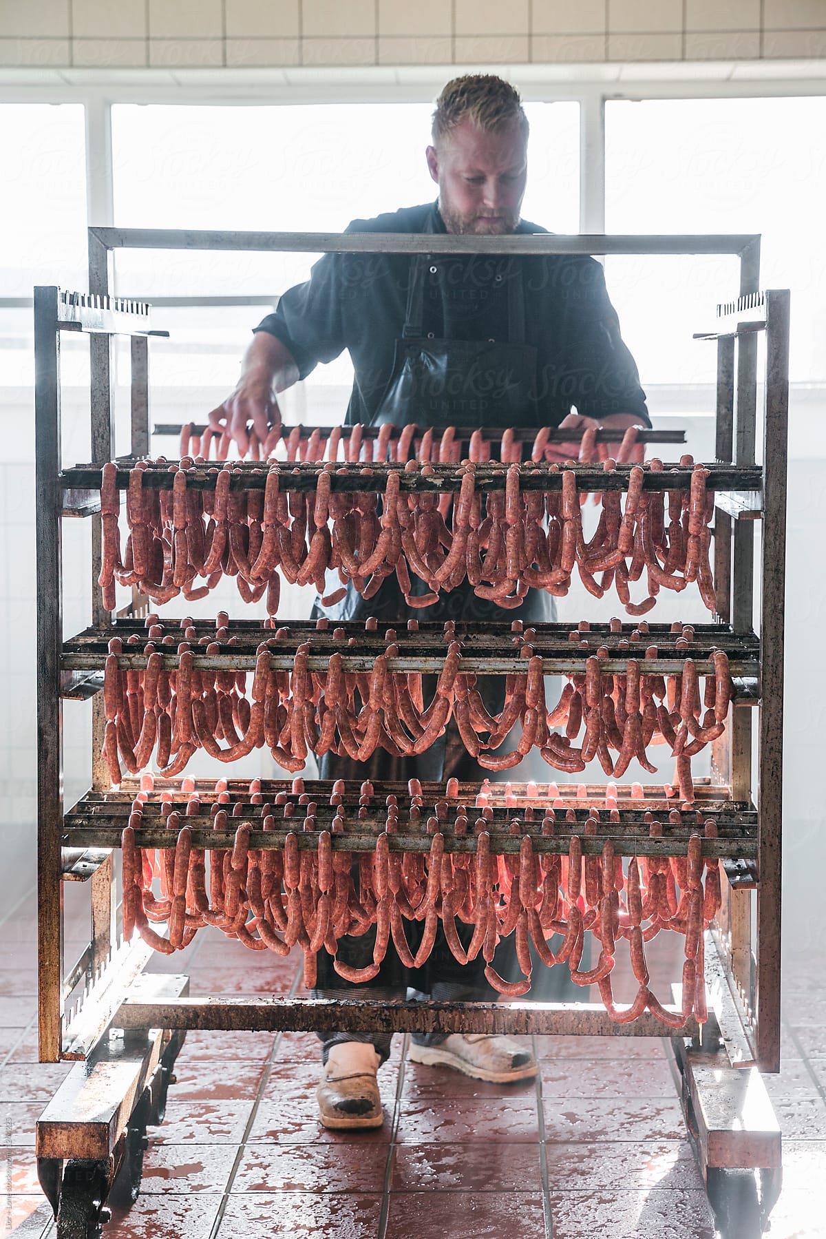 Young butcher adjusting fresh sausages on a smoking rack