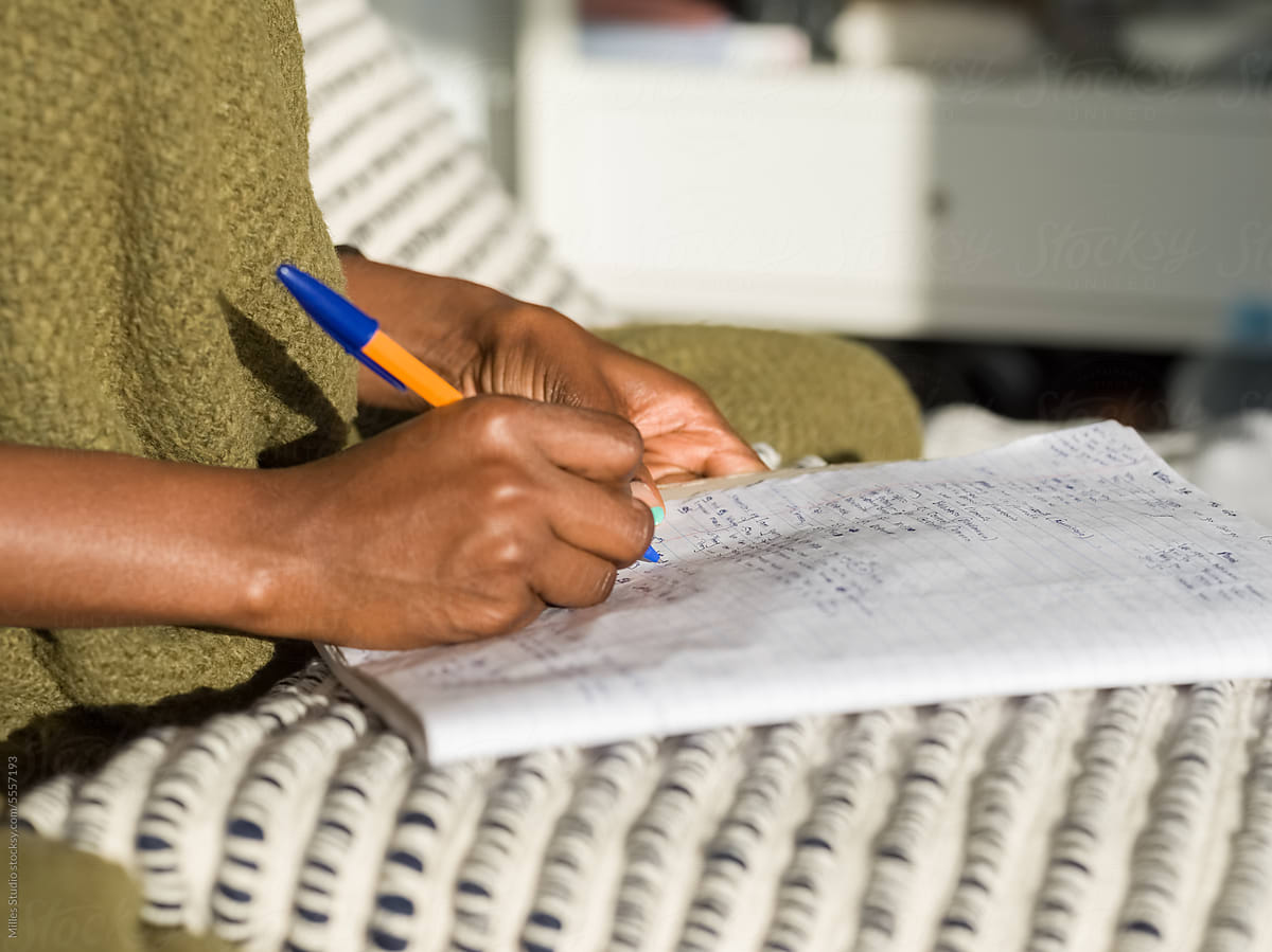 Crop black woman writing Spanish words in notepad