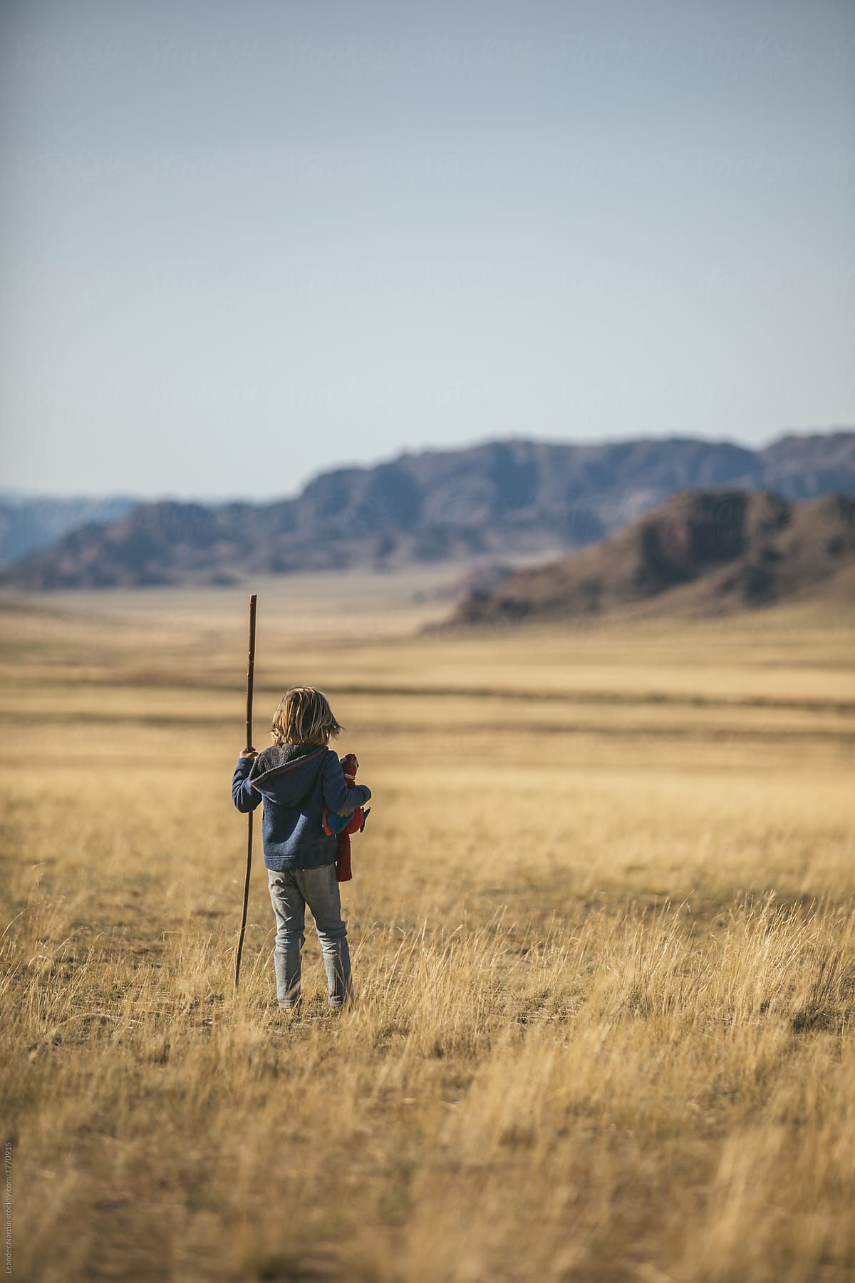 young boy with his plush toy and a big stick wandering in mongolian steppe