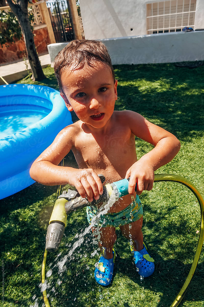 Wet boy playing with water hose in yard on sunny day