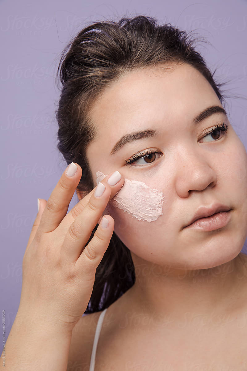 East asian model applying pink cream on her face
