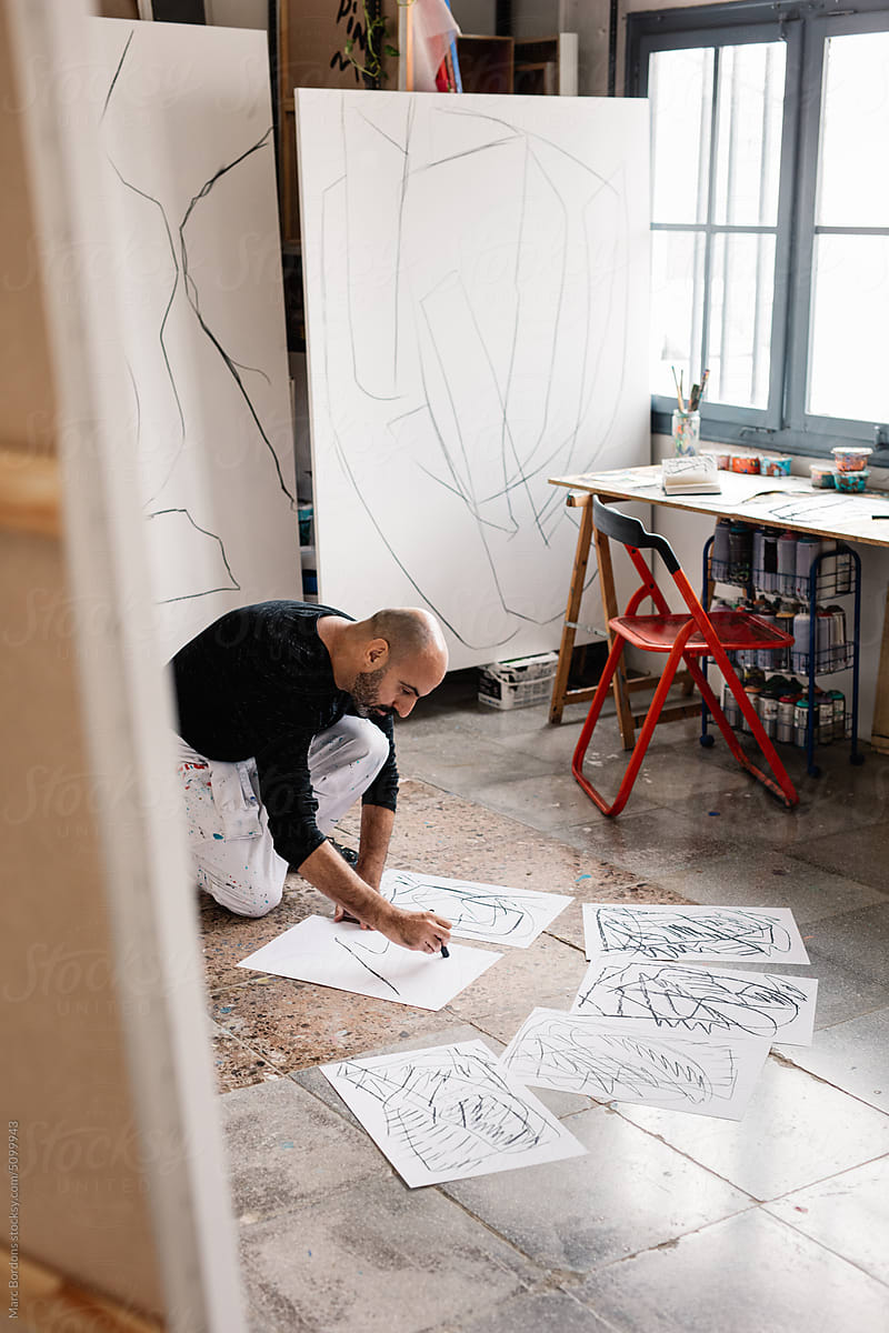 an artist sketches on sheets on the floor of his studio.