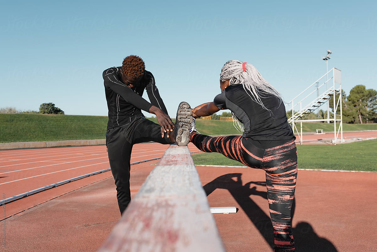 Unrecognizable black athletes stretching legs on barrier