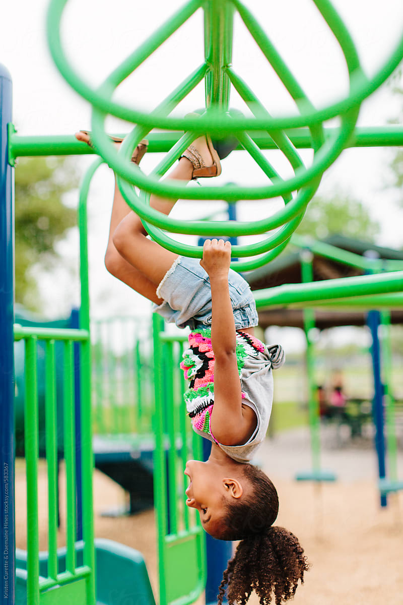 An African American child hanging upside down on the monkey bars & ...