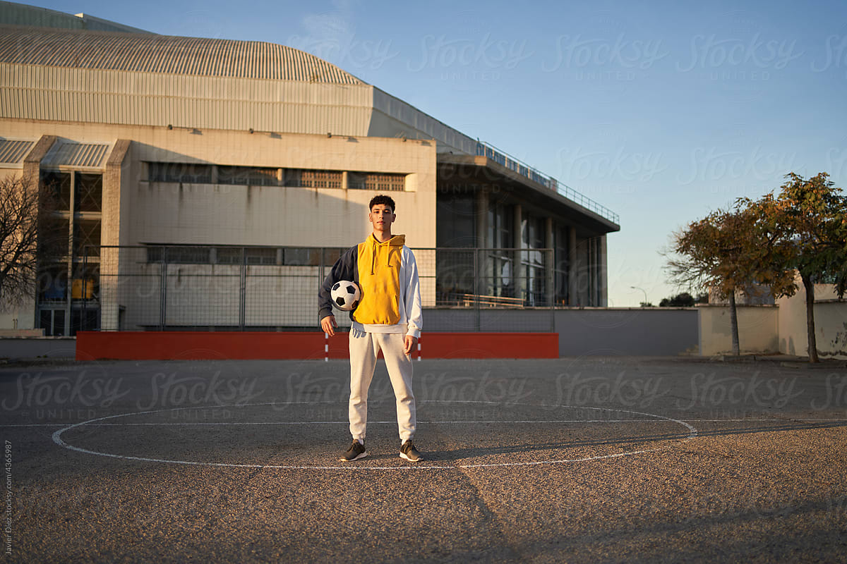 Serious man with soccer ball standing on sports ground