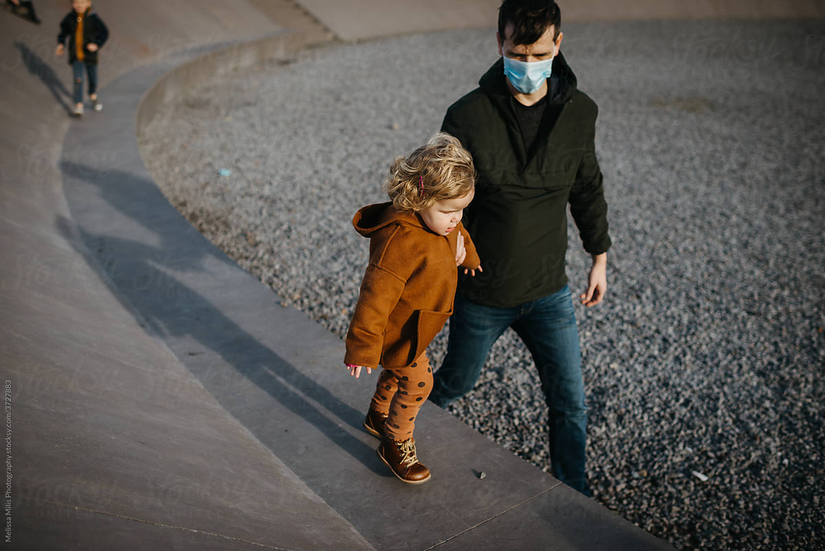 Father with face mask helping daughter walk on a concrete bench outdoors