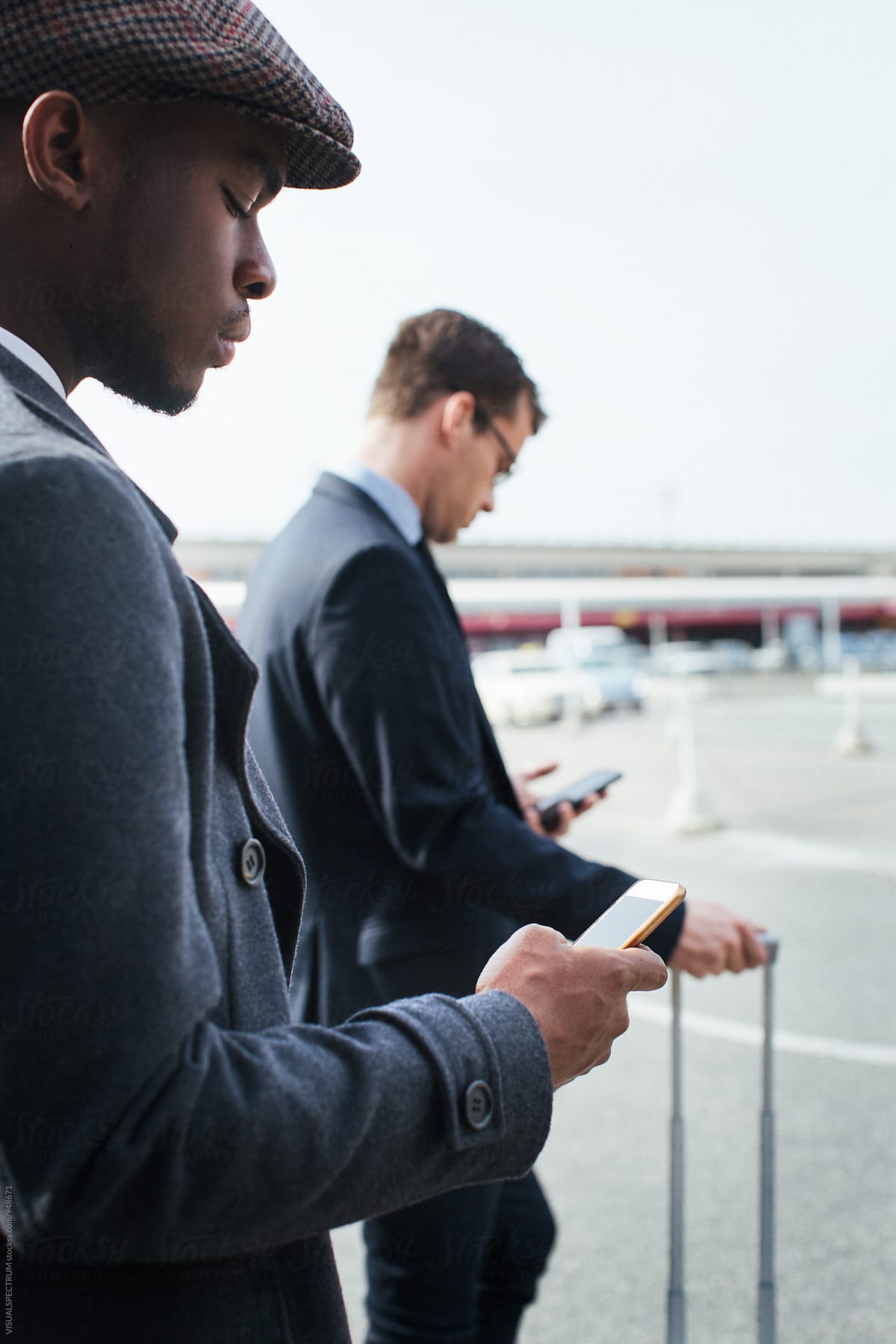 Black and Caucasian Business Travelers Using Smartphones as They Wait For Taxi
