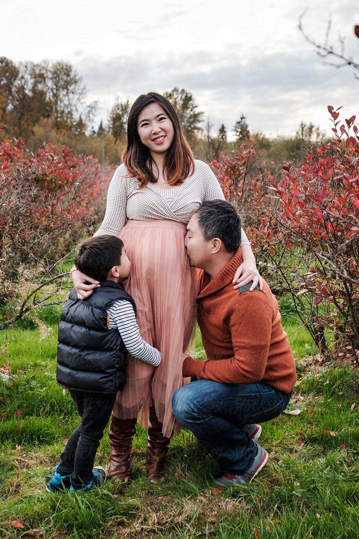 Asian father and son kissing pregnant mother belly