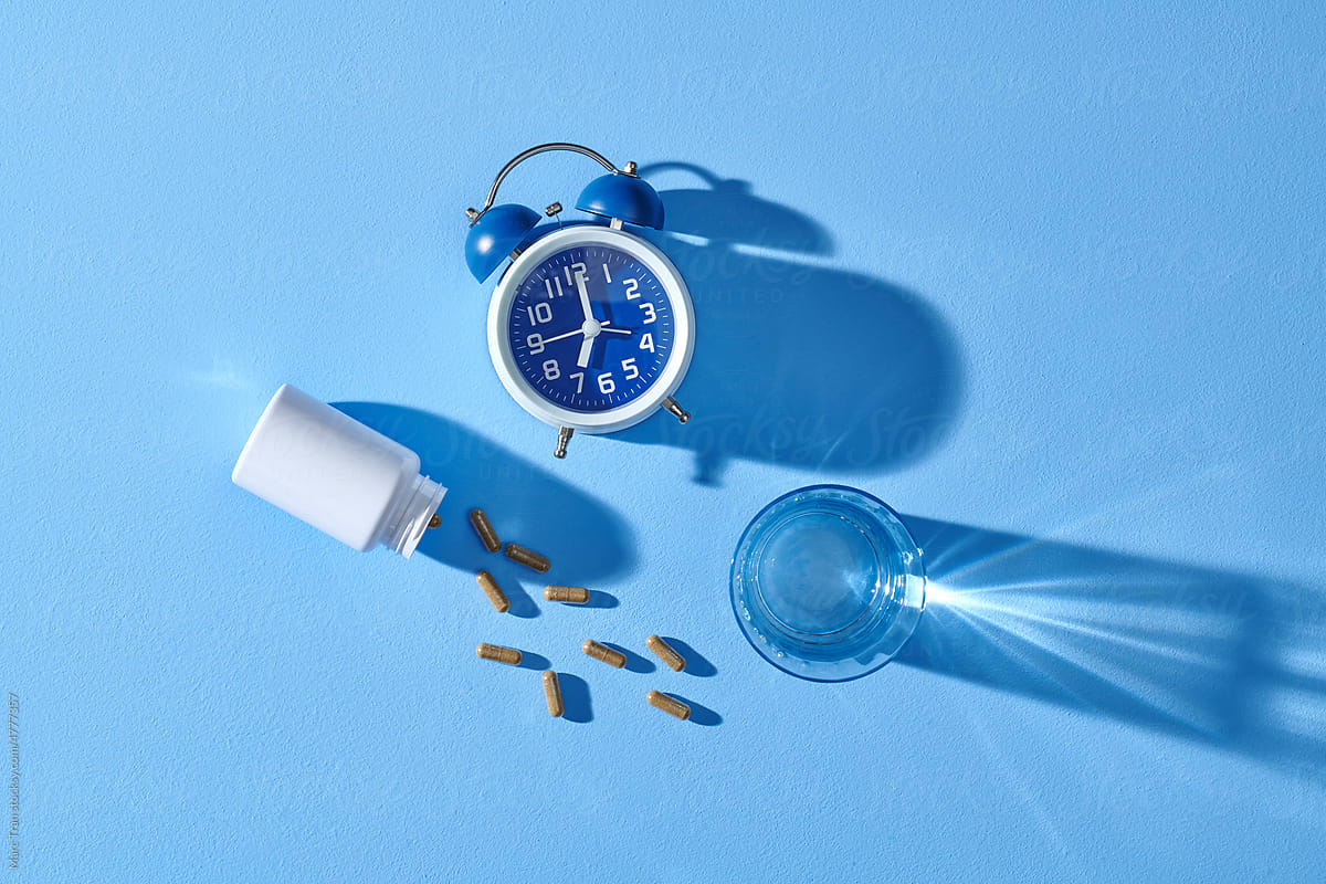 Blue surface with alarm clock, various pills, medicine bottles