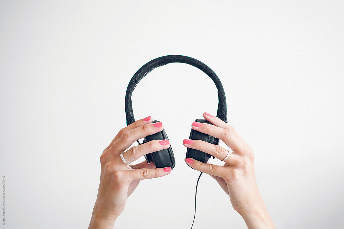 Two Female Hands Holding Up Headphones In Front A White Wall. by Denni Van Huis