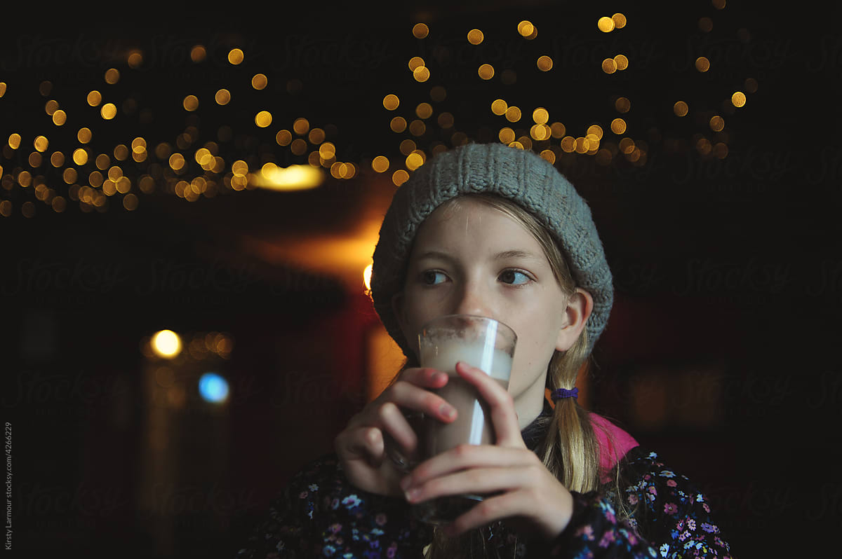 A girl drinks hot chocolate with fairy lights hanging behind her