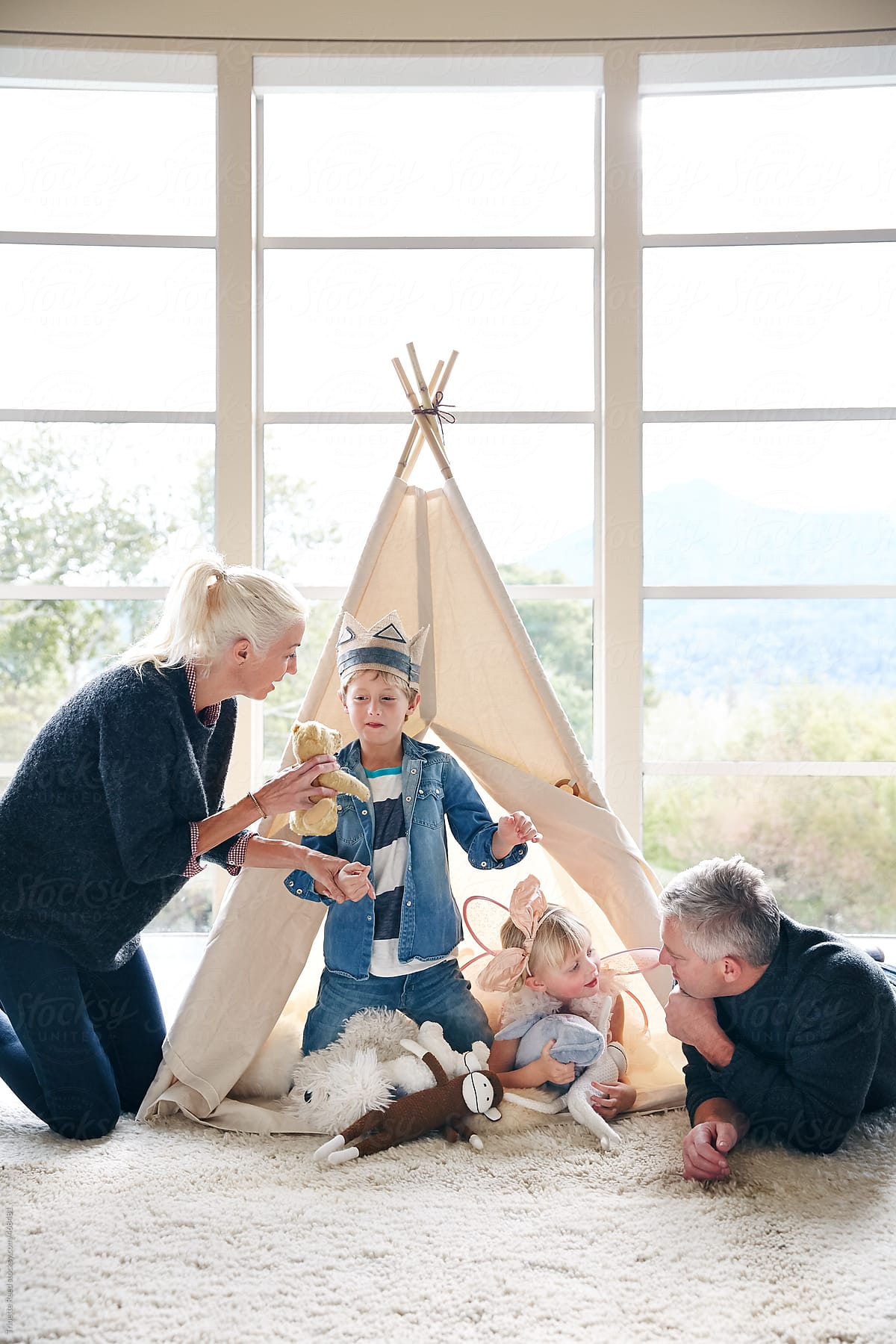 Family playing in teepee tent in living room together.