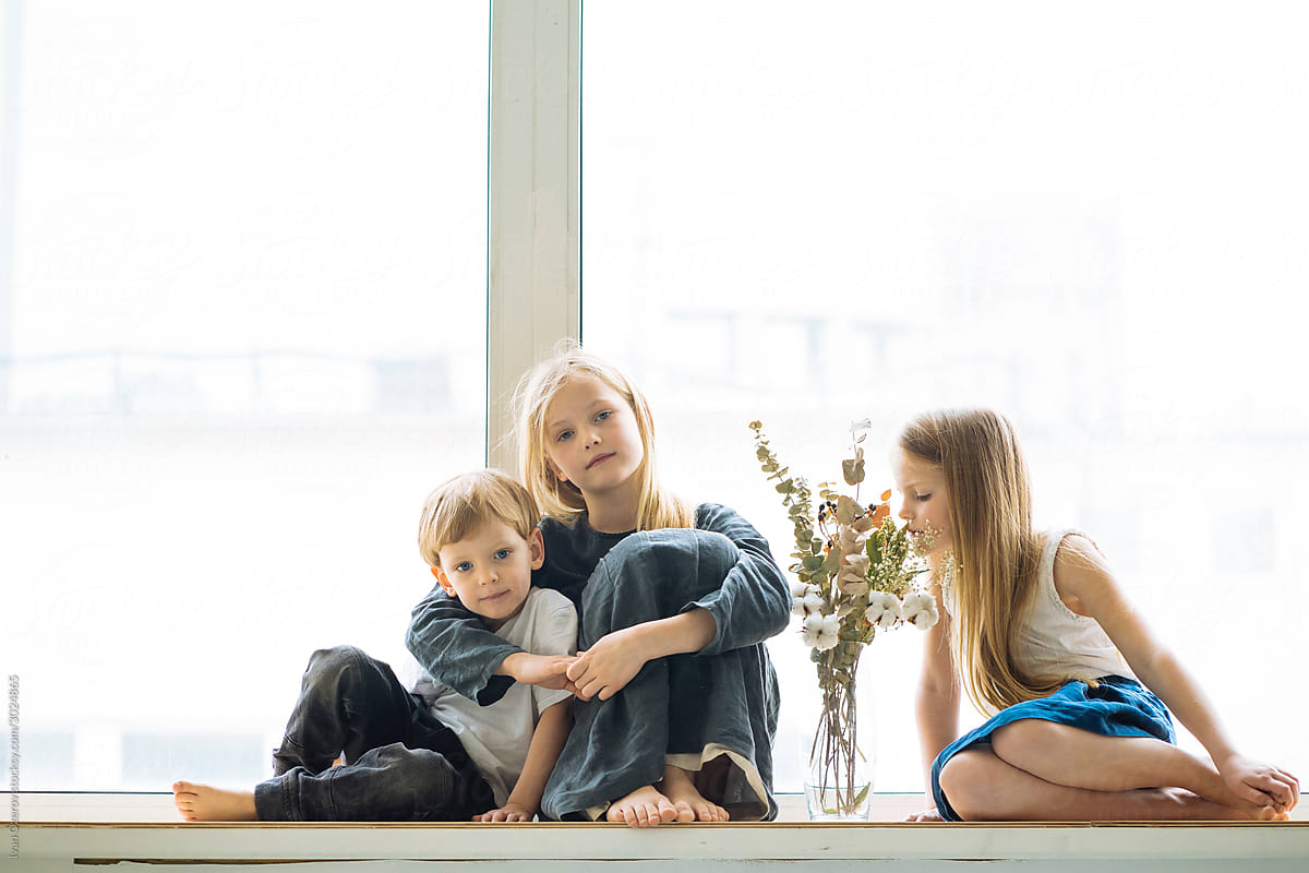 portrait of three children sitting on a windowsill
