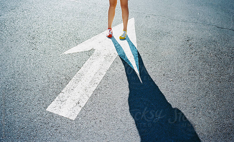 girl in red sock and yellow sock on painted arrow on street