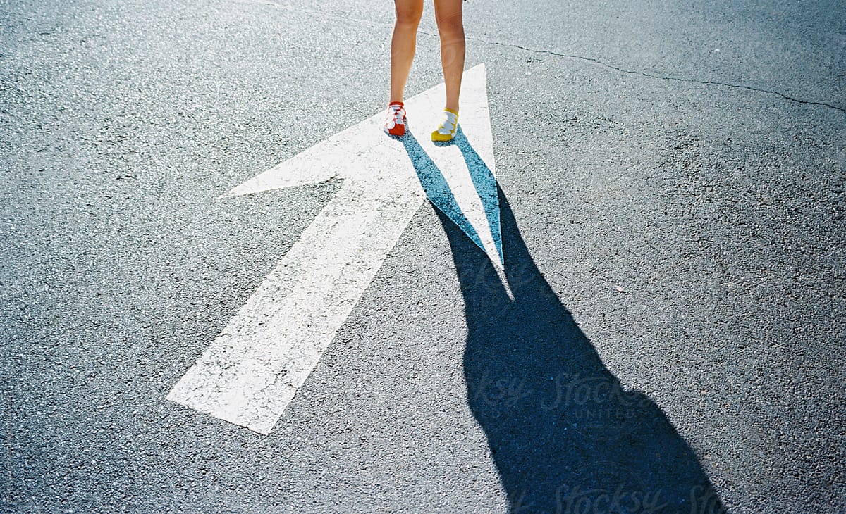 girl in red sock and yellow sock on painted arrow on street