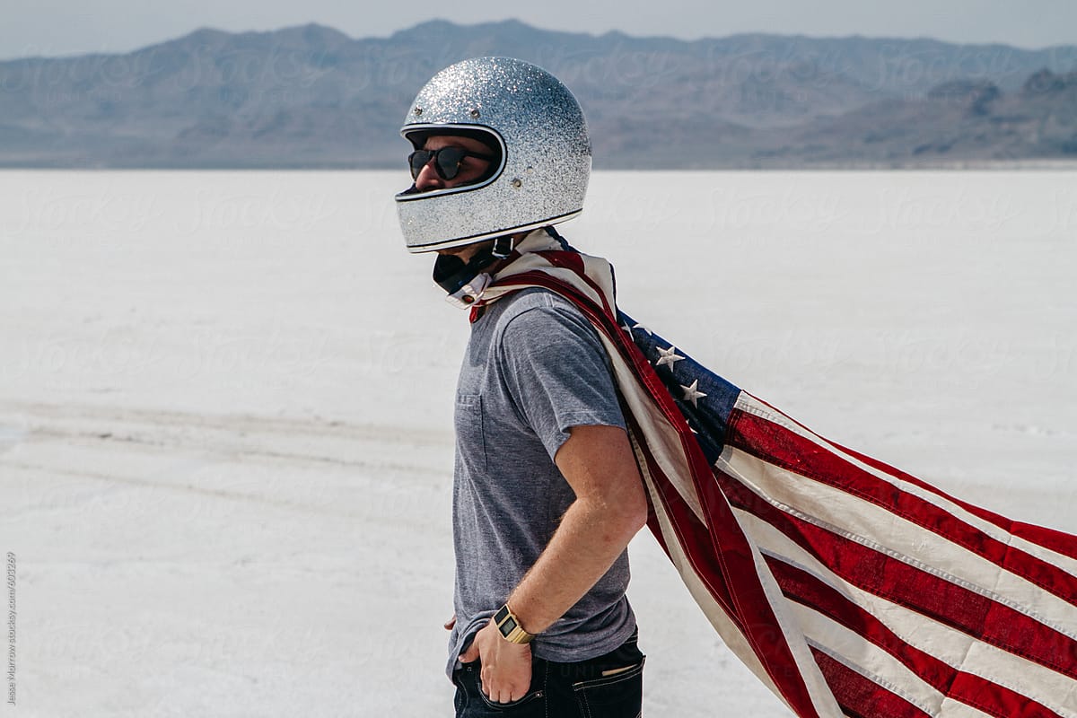 young male wearing motorcycle sparkle helmet and american flag standing in desert salt flat