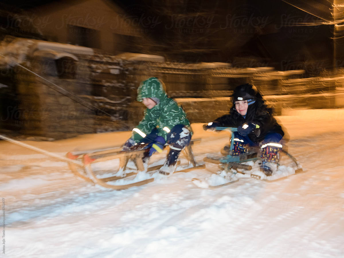 Winter night race of two boys on sleds