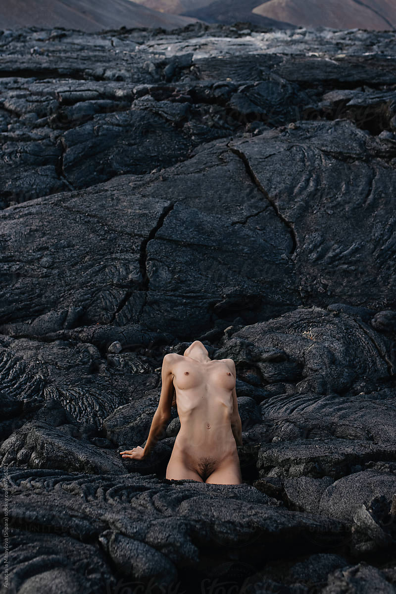 Naked woman leaning on black solid lava in Iceland