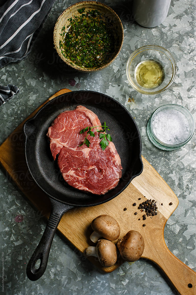 Beef steak in a cast iron pan,surrounded by ingredients for preparing the meat.