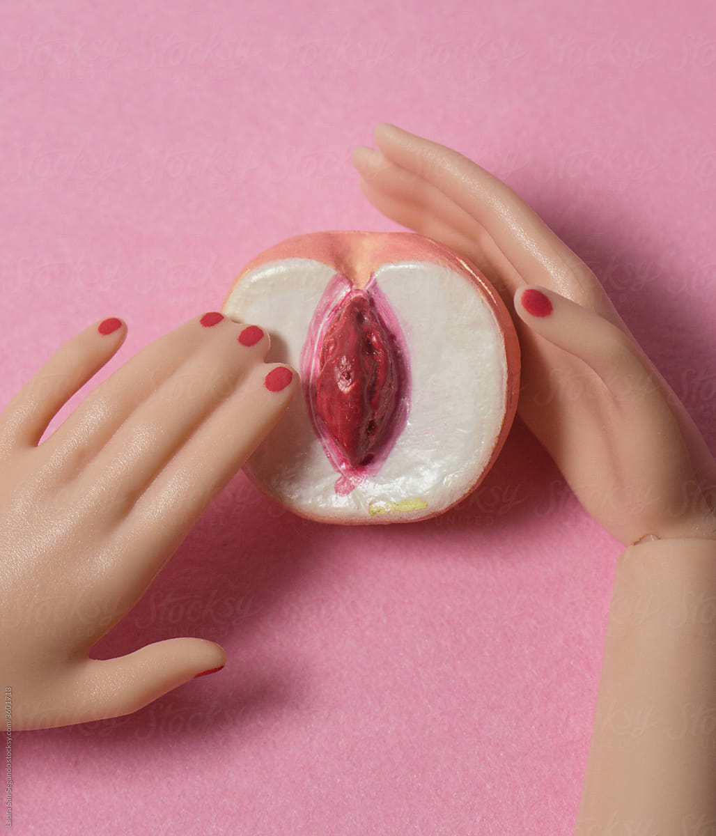 Doll plastic hands with red nails touching an open pink peach.