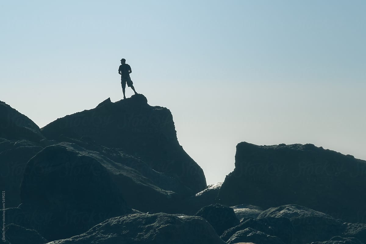 Man silhouetted standing atop large costal boulder