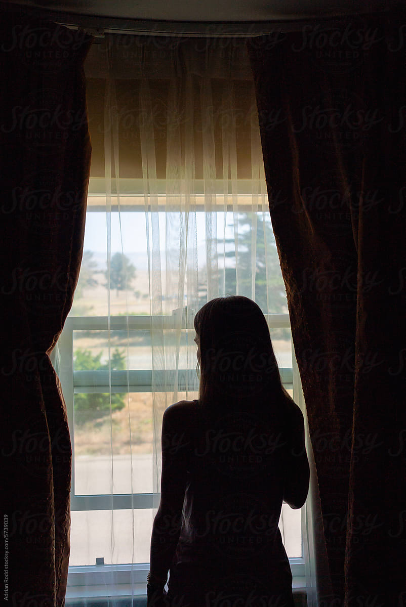 The silhouette of a female figure gazing out through the window