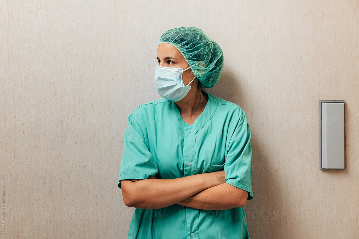 Tired doctor in scrubs and mask standing over wall in hospital