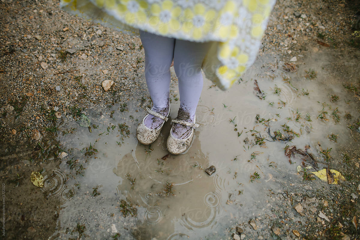 Little girls legs and feet as she jumps in muddy puddles while dressed up in satin, shoes and yellow dress.