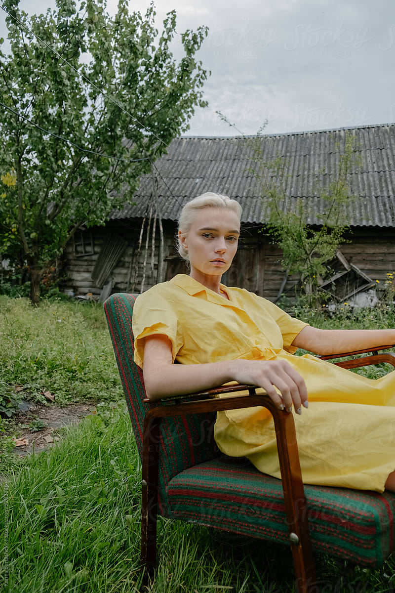 thoughtful girl in a yellow retro dress who sits in a chair in nature