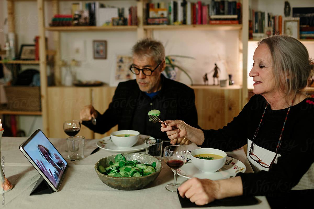 Elderly couple having dinner while video chatting with their daughter on the ipad.