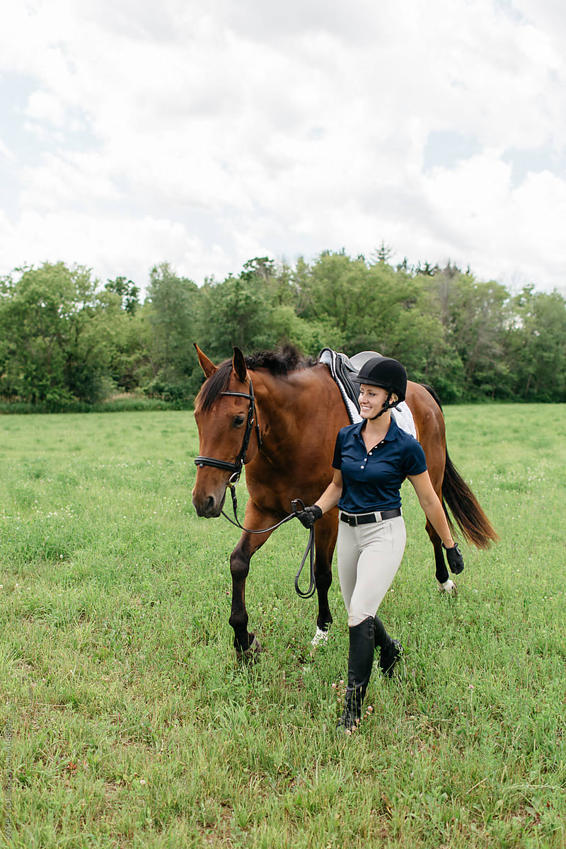 Young female horse rider leading her horse in a field on foot