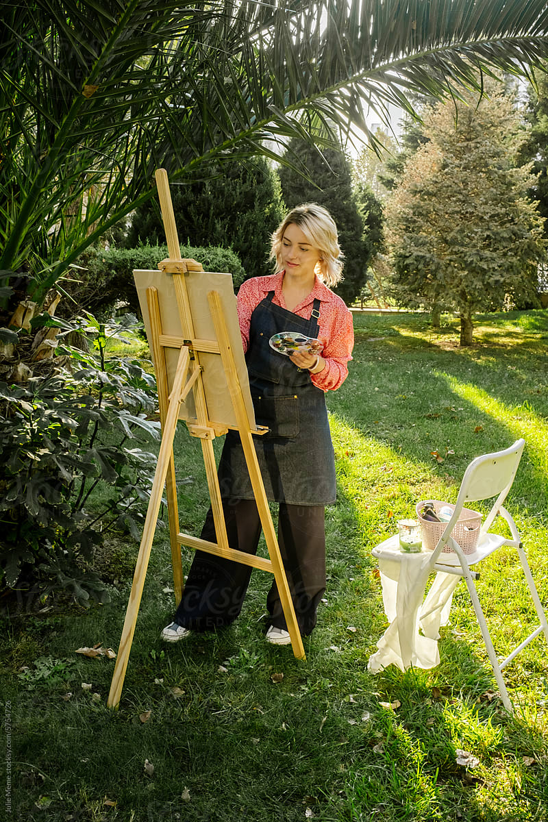 The female artist is painting a picture outdoors in the sunlight