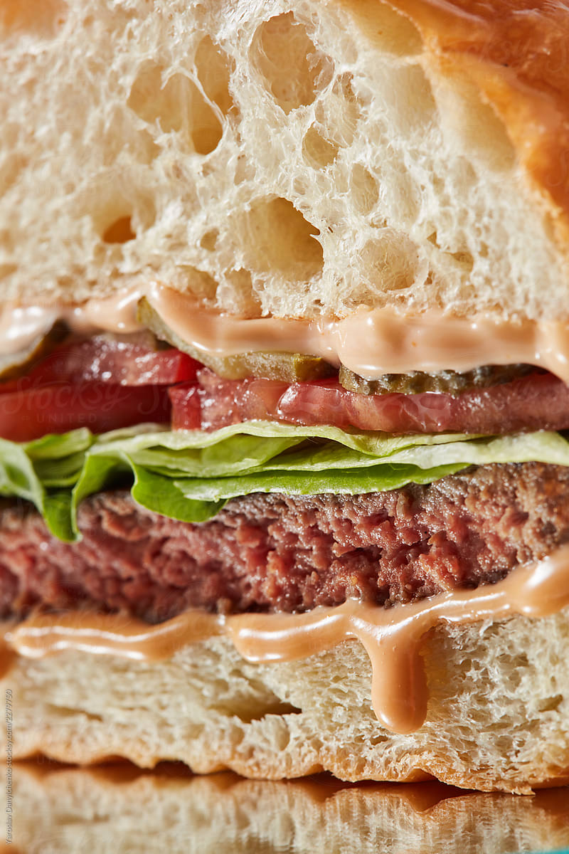 Macro view of tasty grilled beef burger incision background with greenery, sauce, baked bun.