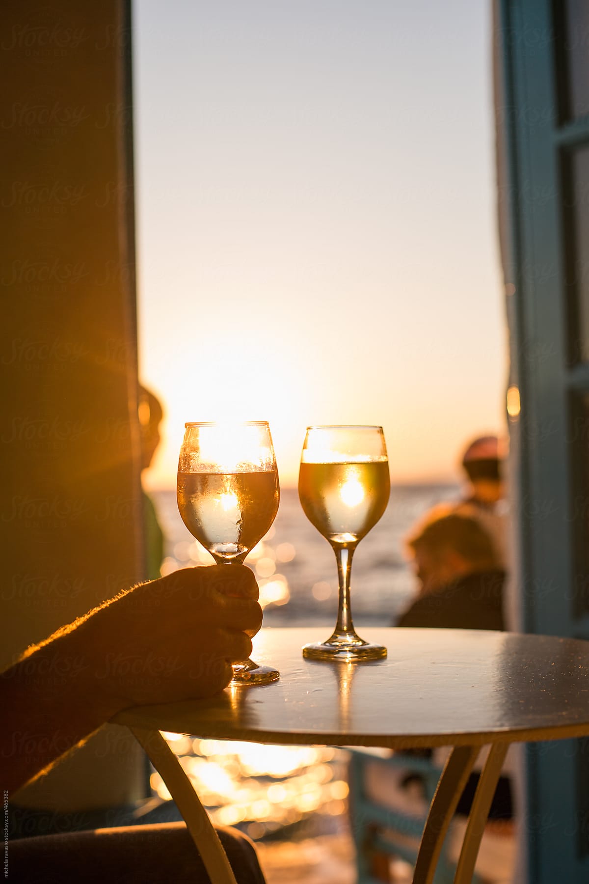 Man holding a glass of white wine at sunset near the sea