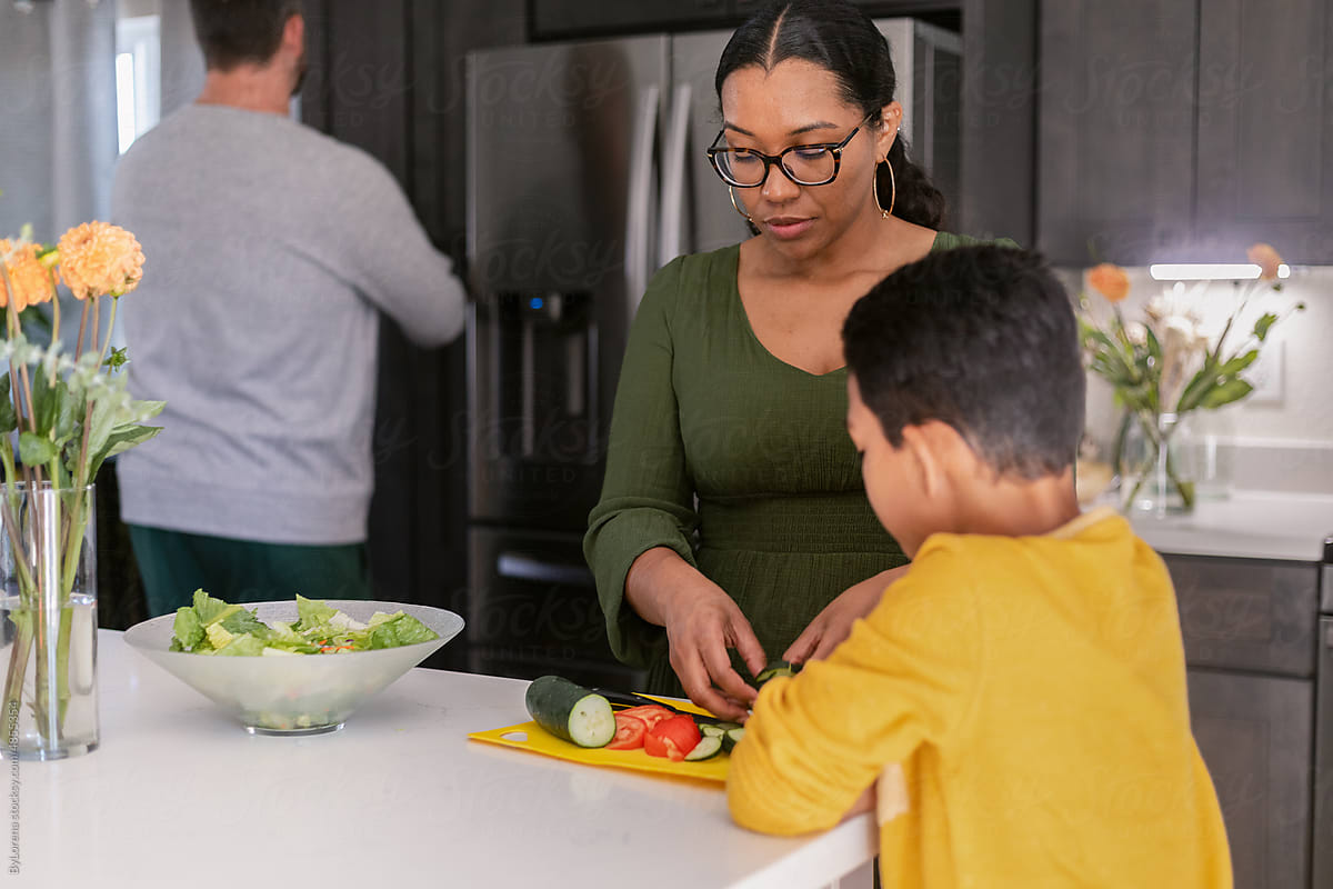 Mother making salad while son eats cucumber