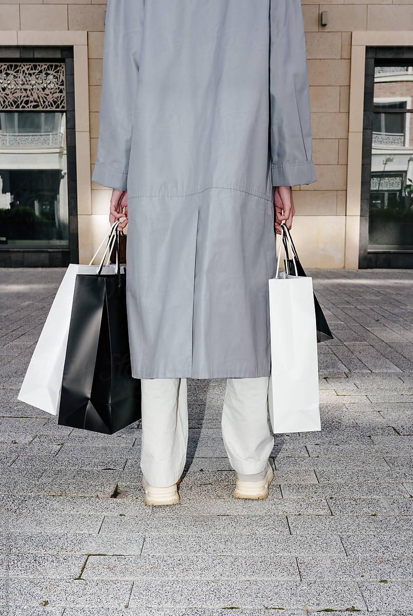 Crop person in coat with shopping paper bags at street