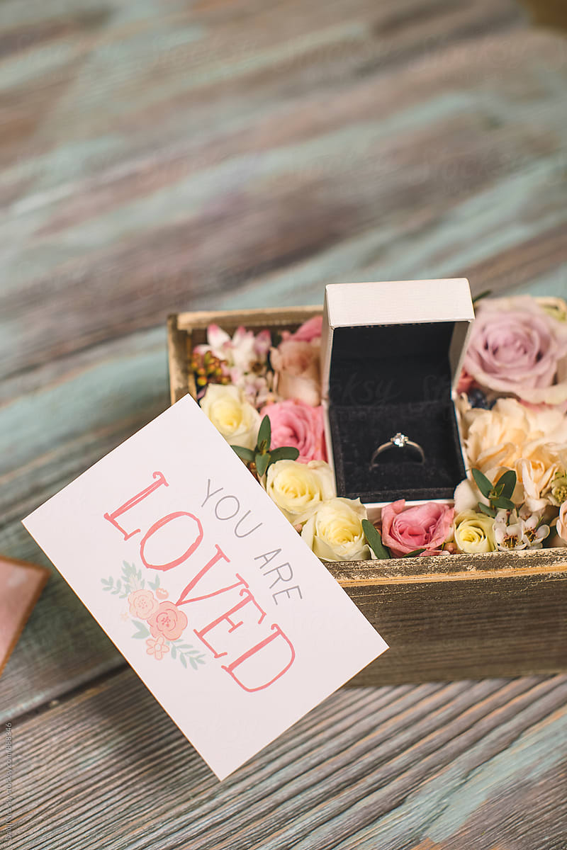 Close-up of ring in box with flowers and 'you are loved' card.
