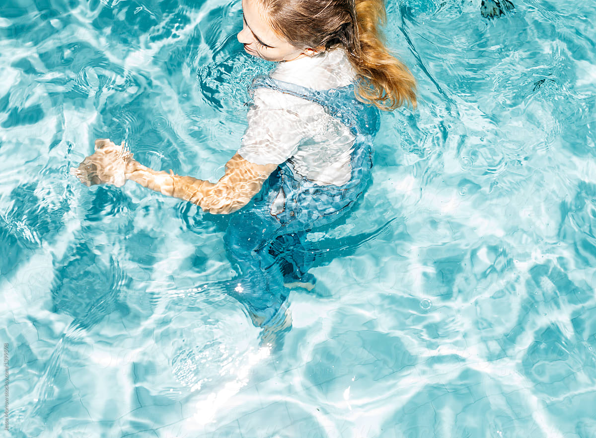 Young woman wearing all her clothes while swimming in pool during night time spontaneous summer swim