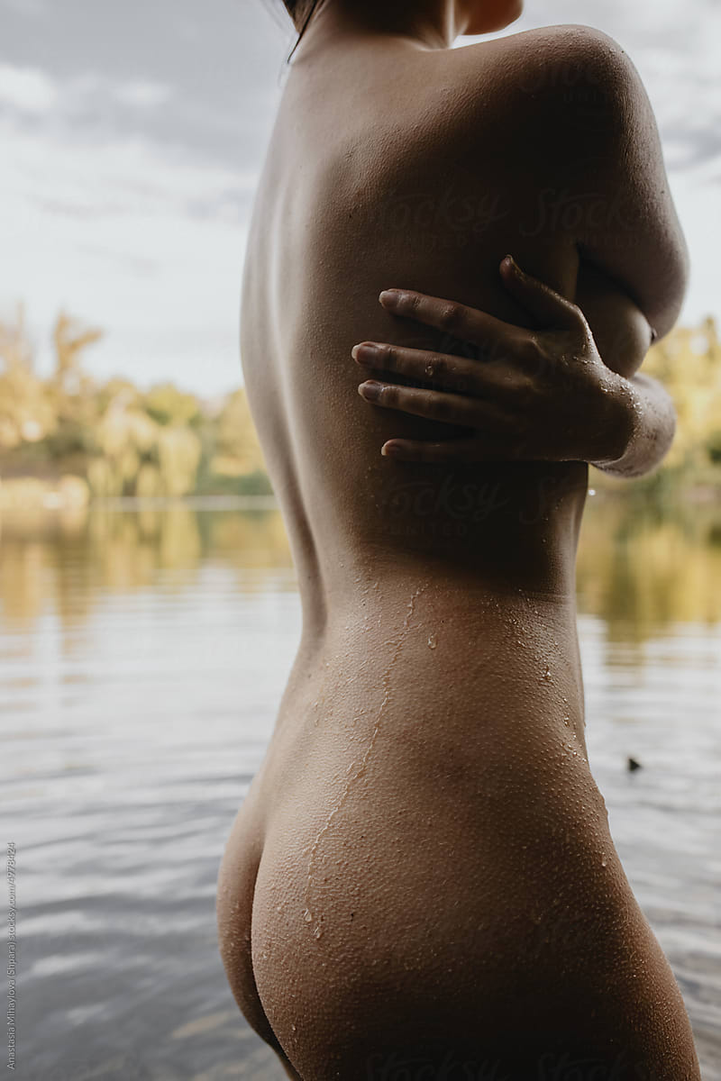 Nude tanned woman posing hugging her back with arms in the lake