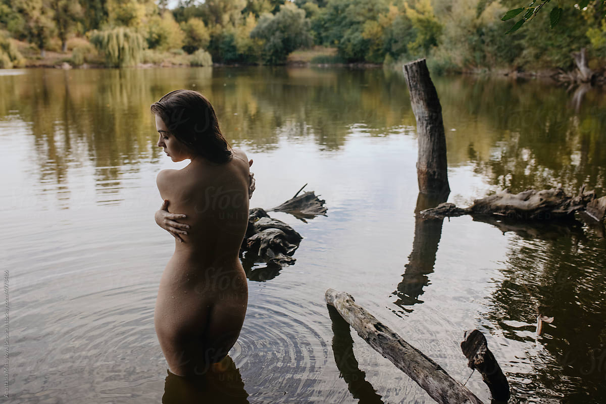 Portrait of nude tanned woman posing from back in the lake