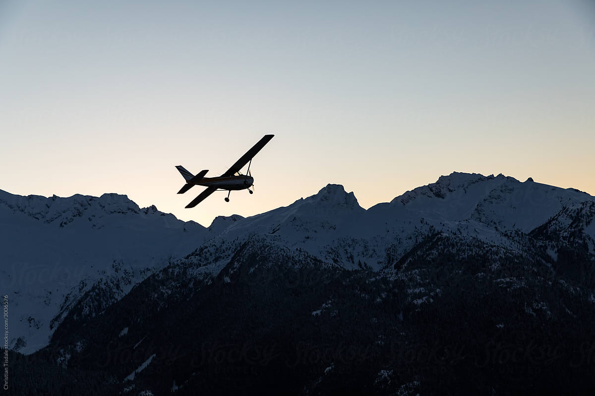 A single engine airplane flying through snowy mountains at sunset